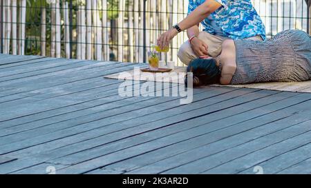 Back view of Asian couple relaxing and chilling with beverage at a riverside. Relaxed lifestyle for lover enjoying freedom together in summer holidays Stock Photo