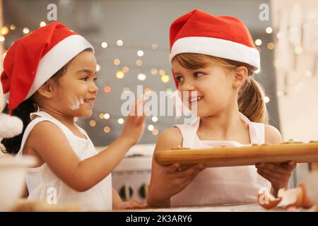 Playful bakers. Two little girls wearing santa hats baking in the kitchen. Stock Photo