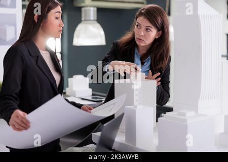 Architects discussing blueprint, holding building construction project draft, coworking in architecture office. Designers teamwork, real estate workers talking about industrial sketch Stock Photo