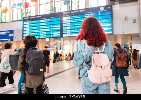 21 July 2022, Dusseldorf, Germany: Girl with backpack looking at info timetable and waiting for delayed train at platform Stock Photo