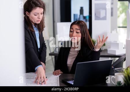 Architects working with blueprints, discussing drafts in coworking space. Employees in architecture office at workplace desk, real estate agency construction project, workers teamwork. Stock Photo
