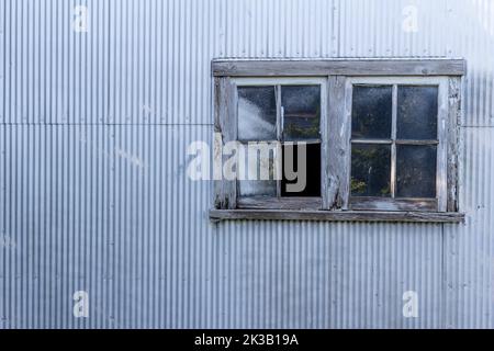 Abstract texture background of a rustic old wood framed glass window on a corrugated metal shed wall, with a grungy shabby chic appearance Stock Photo