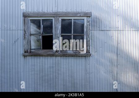 Abstract texture background of a rustic old wood framed glass window on a corrugated metal shed wall, with a grungy shabby chic appearance Stock Photo