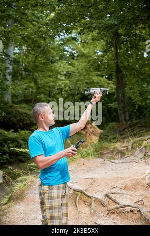 Man operating drone using remote controller. Man using drone for photos and video making while standing in green forest. Stock Photo