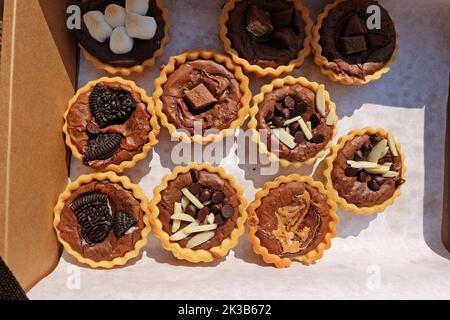 Close up paper box of Chocolate fudge brownie tarts topped with Sliced Almond sticks, Marshmallow, Sugar bar and peanut butter Stock Photo