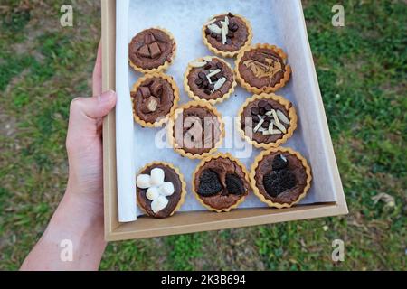 Close up paper box of Chocolate fudge brownie tarts topped with Sliced Almond sticks, Marshmallow, Sugar bar and peanut butter Stock Photo