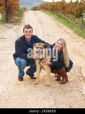Hes like a child to them. Portrait of a young couple with their pet Alsatian on a wine farm. Stock Photo