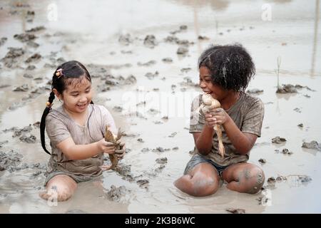 Two happy children child girl catching big frog in the large wet mud puddle on summer day. Stock Photo