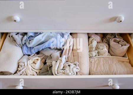 Storage of mess children s clothes in a drawer of a white chest, open closet shelf close-up with clutter clothes Stock Photo