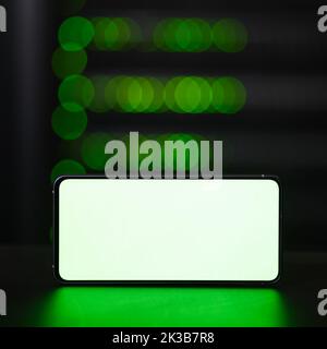 Empty blank with a white background on the phone screen, copy space. Smartphone on the background of a dark server room, mockup Stock Photo
