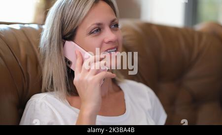 Pretty woman is sitting on couch talking on mobile phone Stock Photo