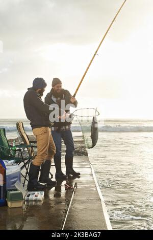 Fishings a team effort. two young men fishing off a pier Stock Photo - Alamy