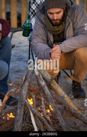 Camping out on the beach. A young man making a fire on the beach. Stock Photo