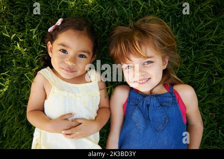 Too cute. High angle portrait of two little girls lying on the grass. Stock Photo