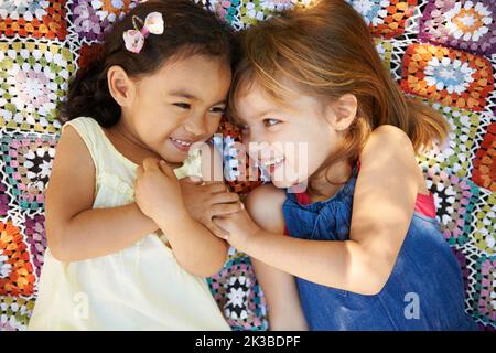 Warning This image may cause broodiness in even the most cynical of viewers. High angle shot of two little girls lying down and playing on a blanket. Stock Photo