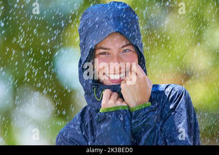 Flirting with the rain. a young woman standing happily in the rain with her raincoat. Stock Photo