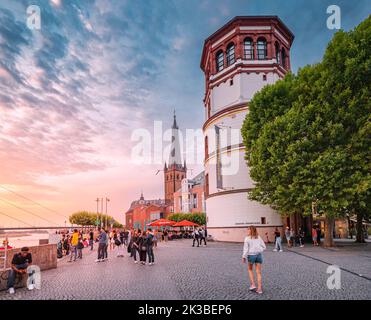 22 July 2022, Dusseldorf, Germany: People walking by promenade and admiring sunset view of Dusseldorf city old town Towers in Altstadt. Travel and vis Stock Photo