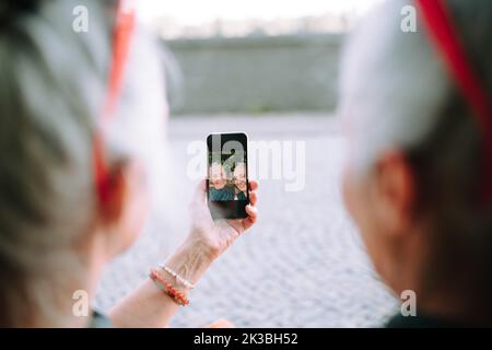 Senior women twins outdoors in city park taking and chcecking selfie. Stock Photo