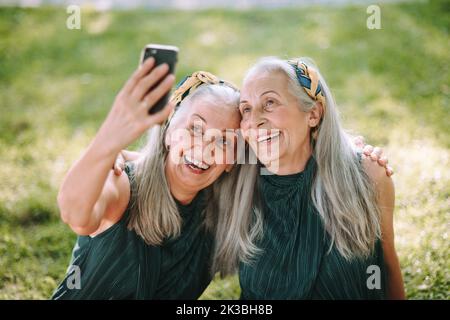 Senior women twins outdoors in city park taking selfie. Stock Photo