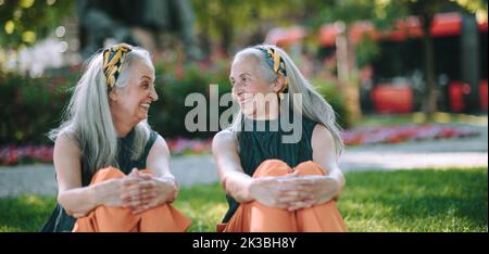 Happy seniors women, twins sitting in city park, smiling and talking. Stock Photo