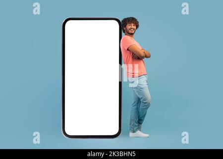 Cool hindu guy leaning on big cell phone, mockup Stock Photo