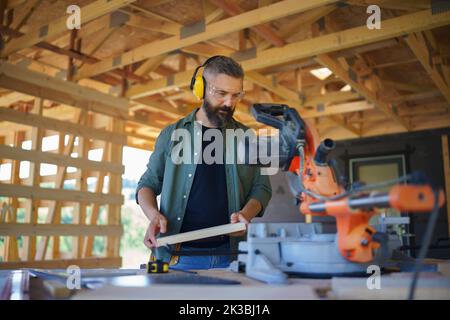 Construction worker working with eletric saw inside wooden construction of house, diy eco-friendly homes concept. Stock Photo