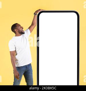 African American Man Touching Big Phone Standing On Yellow Background Stock Photo