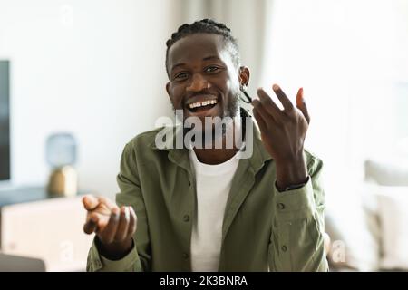 Video call concept. Happy african american man talking to camera, gesturing and smiling, sitting at workplace at home Stock Photo
