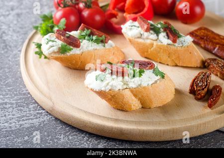 Canape, crostini with toasted baguette, cream cheese, sun-dried tomatoes, herbs on plate. Hand-made tasty sandwiches for breakfast. Stock Photo