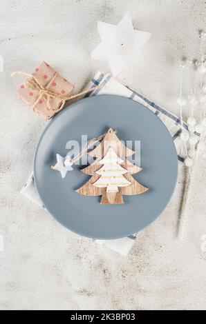 Christmas table setting. Top view of empty grey plate with black cutlery and craft wooden decorations on light table. Event table decoration. Stock Photo