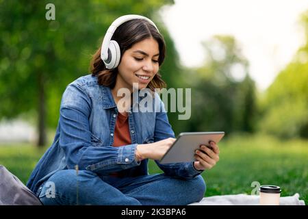 Young Middle Eastern Woman In Wireless Headphones Relaxing Outdoors With Digital Tablet Stock Photo