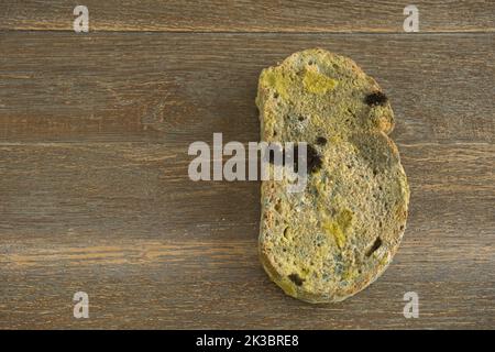 a slice of moldy bread in an upright position on a wooden floor Stock Photo