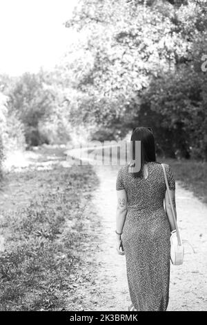 Grayscale photo of a woman walking by a path through the forest Stock Photo