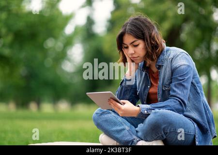Bored Middle Eastern Female Student Sitting With Digital Tablet On Bench Outdoors Stock Photo