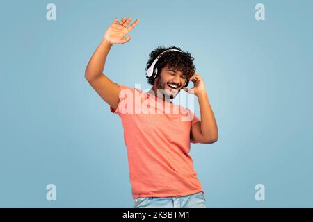 Carefree indian guy listening to music and dancing, using headphones Stock Photo
