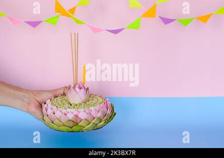 Pink lotus petal krathong that have 3 incense sticks and candle decorates with lotus and crown flower holding by hand for Thailand Loy Krathong festiv Stock Photo