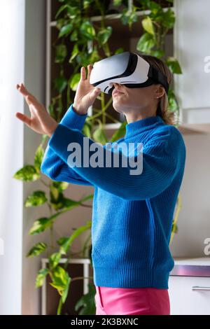 Young woman using VR goggles in cozy interior with plants, hand control, futuristic technologies Stock Photo