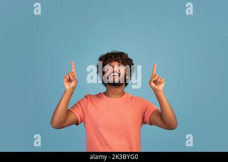 Cheerful hindu guy pointing at copy space on blue Stock Photo