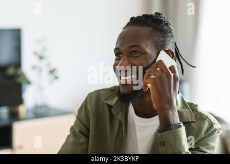Happy african american man talking on smartphone and smiling, having pleasant phone conversation at home Stock Photo