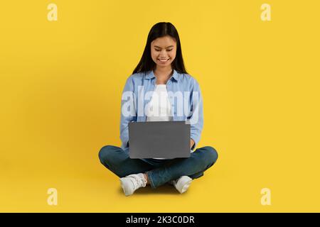 Happy young korean female student in casual typing on laptop, watch online lesson, chatting Stock Photo