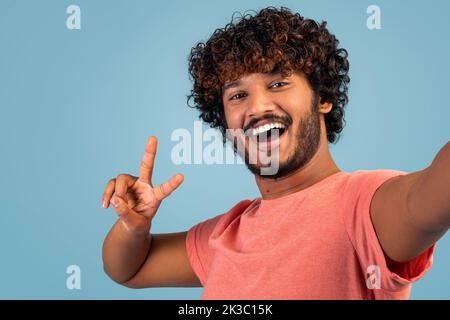 Positive handsome indian guy taking selfie on blue Stock Photo