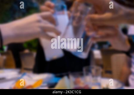 Blurred group of young people clinking Turkish raki glasses, copy space, traditional Turkey appetizers on the background, friends on Turkish pub Stock Photo