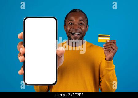 Happy black man holding smartphone and credit card, mockup Stock Photo