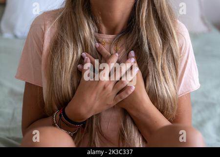 A heartbroken woman holding her chest with her hands while sitting on a bed Stock Photo