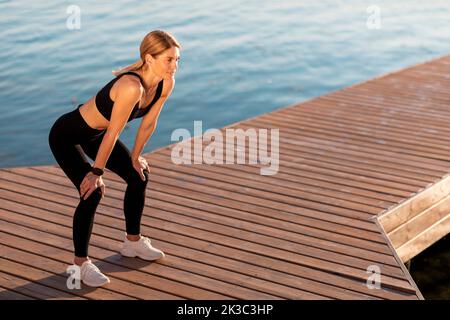 Middle Aged Female Athlete In Activewear Resting On Pier While Training Outdoor Stock Photo