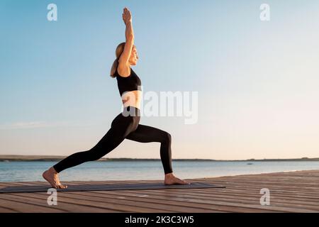 A middle aged woman practicing yoga barefoot outside in a grassy park. She  is wearing a bright orange vest and black leggings. The style of yoga she i  Stock Photo - Alamy