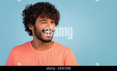 Cheerful handsome young eastern man winking on blue Stock Photo