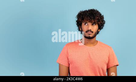 Curious indian guy looking at copy space over blue background Stock Photo