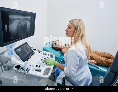 doctor making ultrasonography to male child patient at ultrasound office of medical clinic. Ultrasound diagnostics of thyroid gland for children Stock Photo