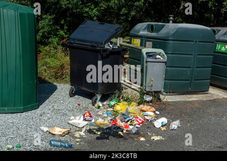 Overflowing trash bin with scattered litter beside recycling containers in a public area Stock Photo